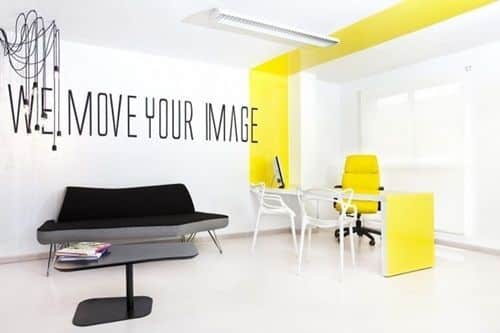 Escritório clean com faixa amarela e adesivos de objetivo. Luminárias industriais e design moderno.